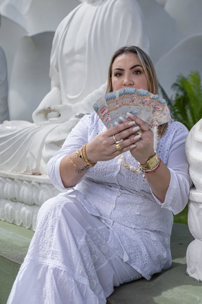 Bruna segurando leque de cartas de Tarot em frente a estátua de Buda